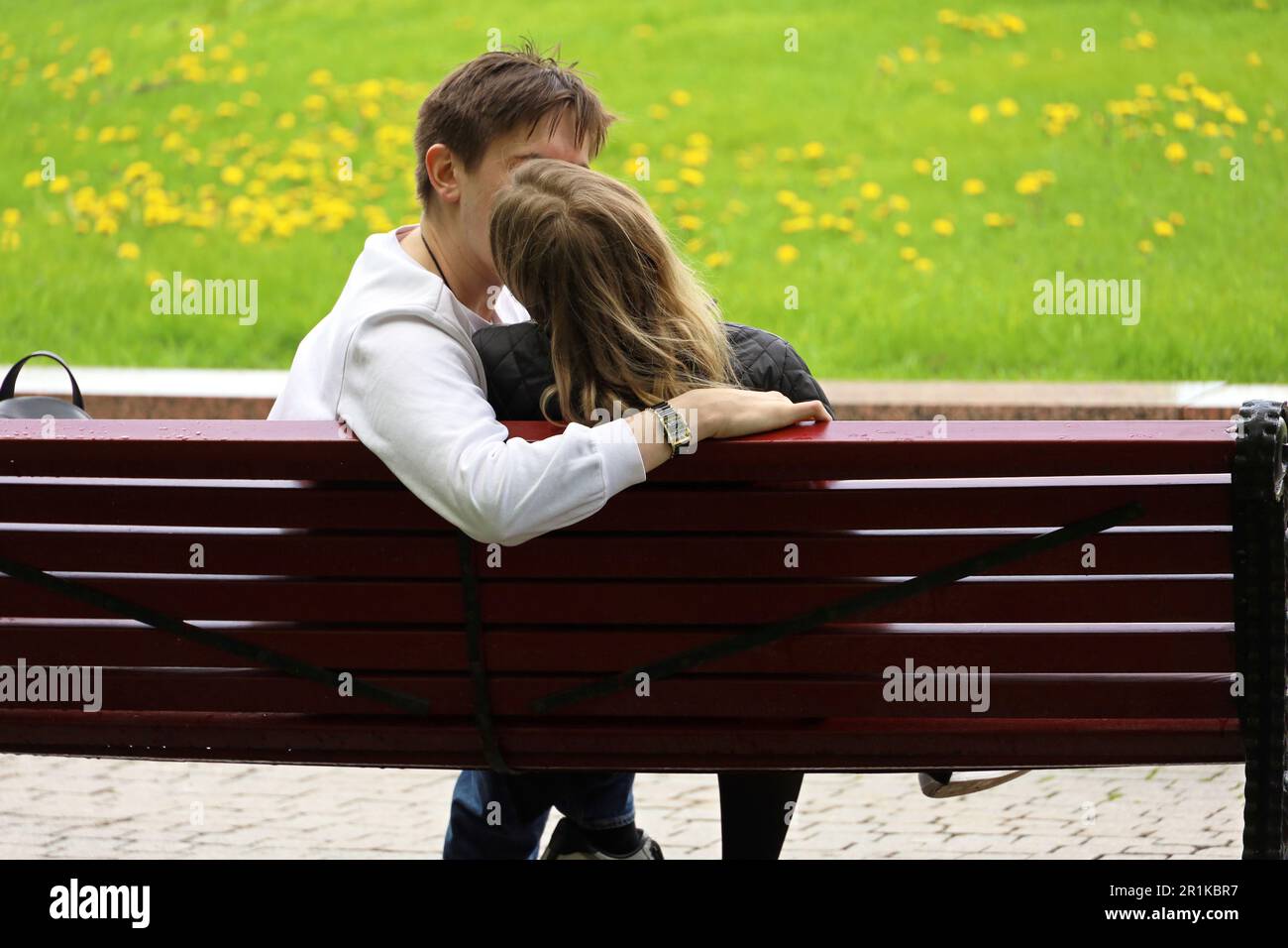 Young couple kissing on a city street. Girl and guy embracing sitting on a bench in spring park Stock Photo