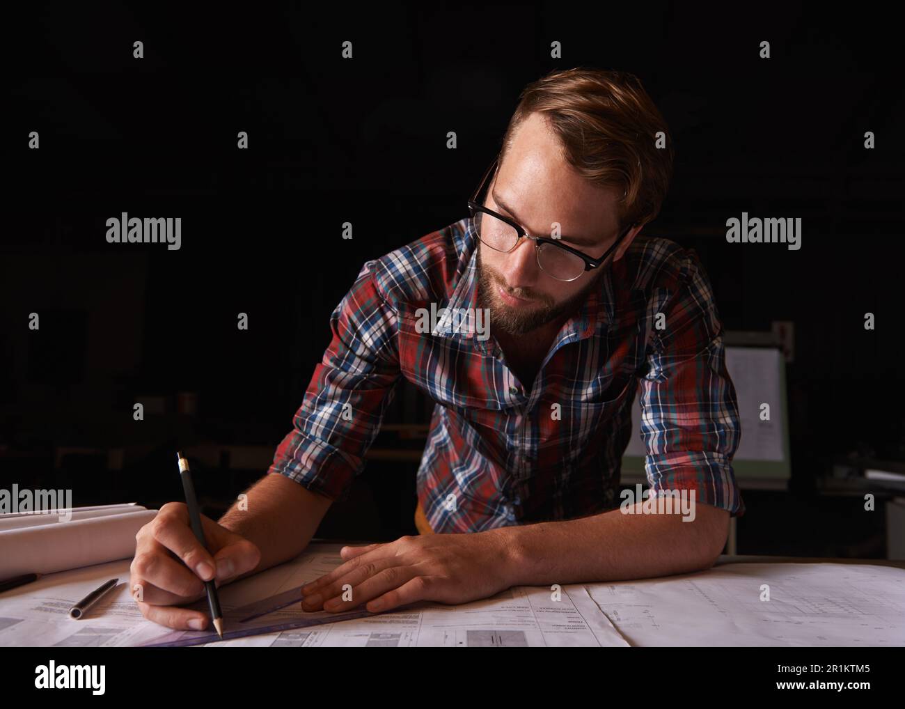 He desired to make the world beautiful. a young man sitting indoors working on building plans. Stock Photo