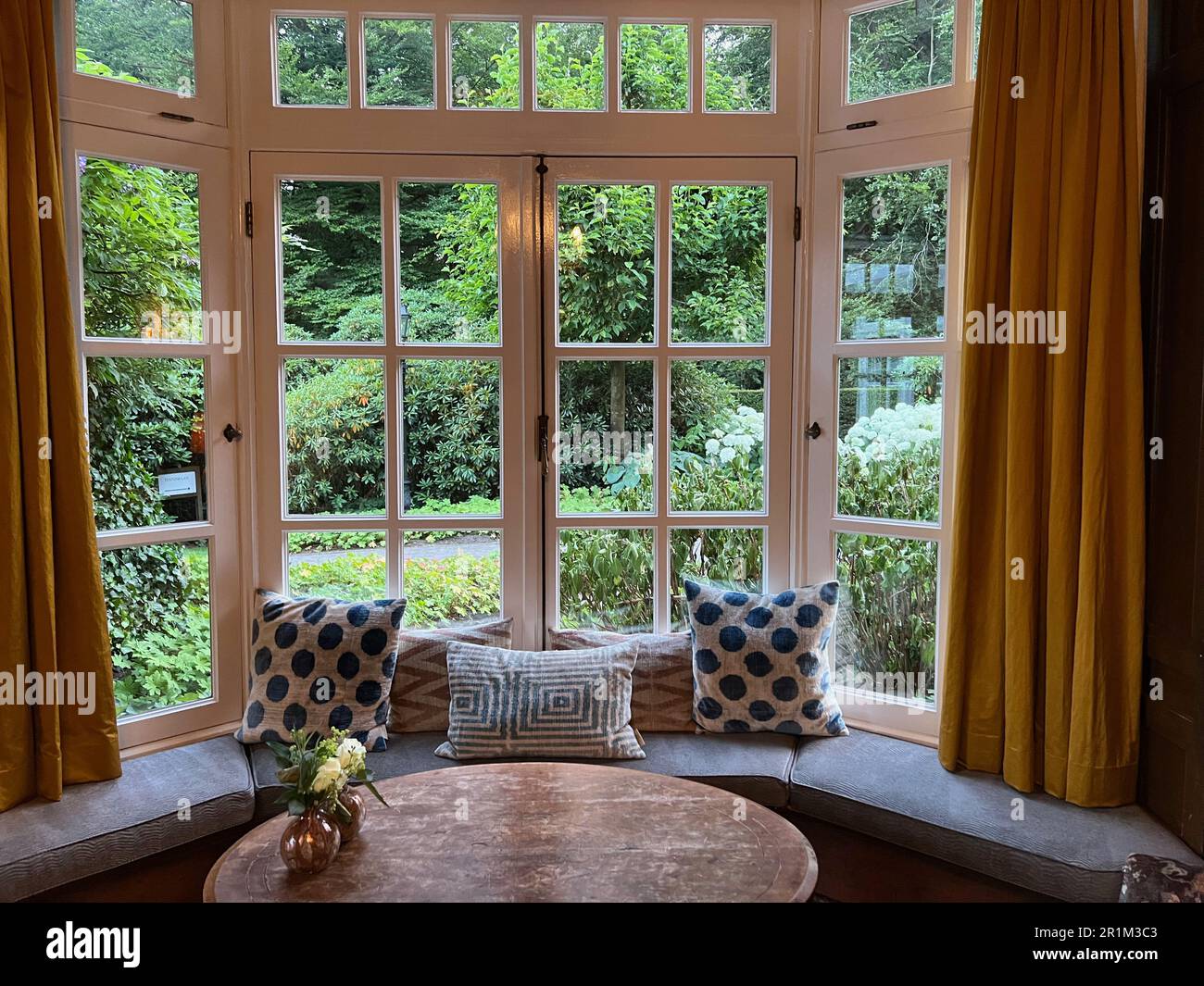 Wooden table near bay window seat with cushions in cozy room. Interior ...