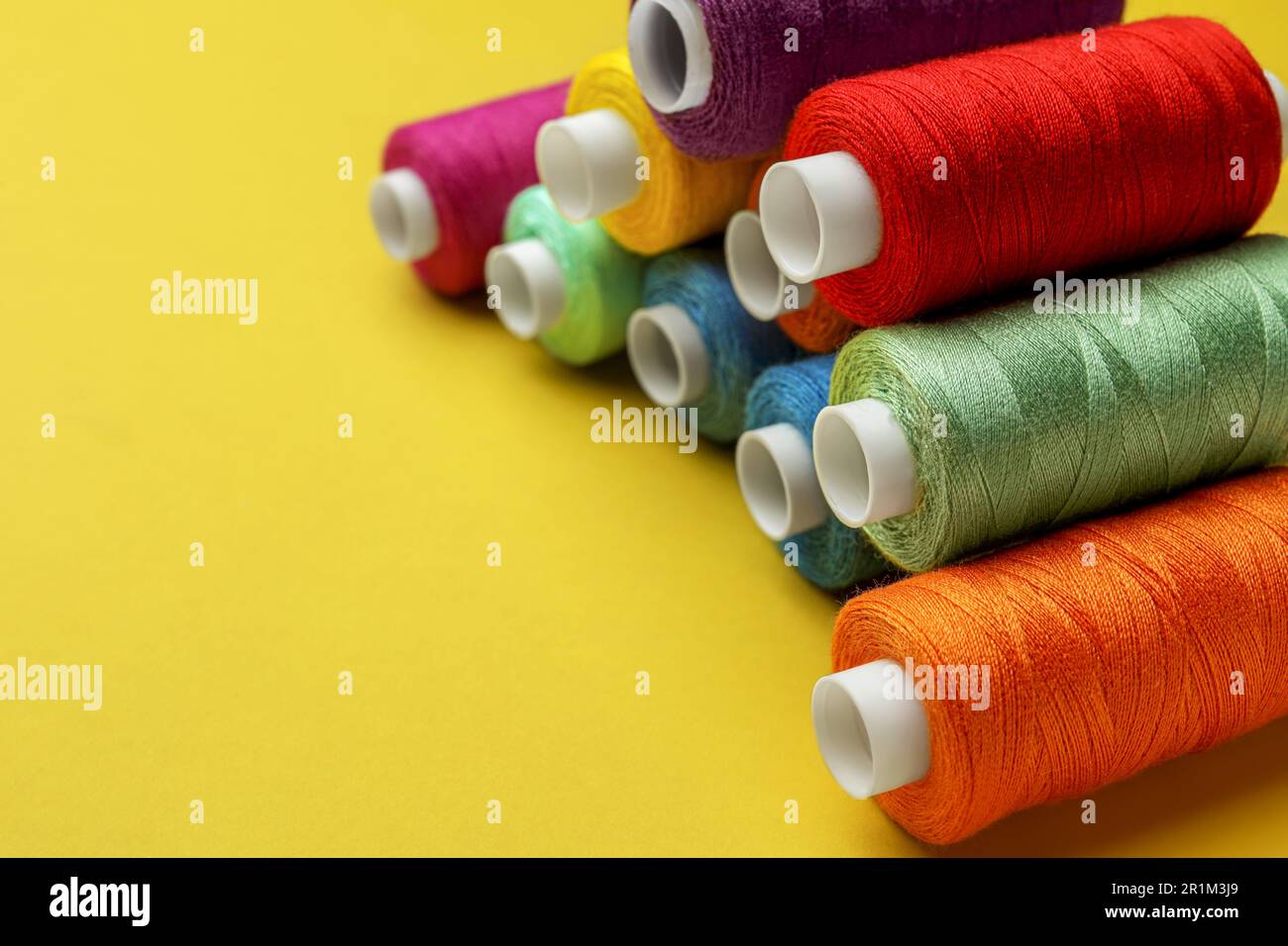 Different colorful sewing threads on yellow background, closeup. Space ...