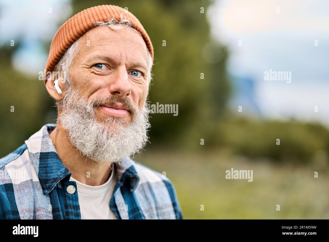 Older elder hipster man standing in nature park wearing earbud. Portrait Stock Photo