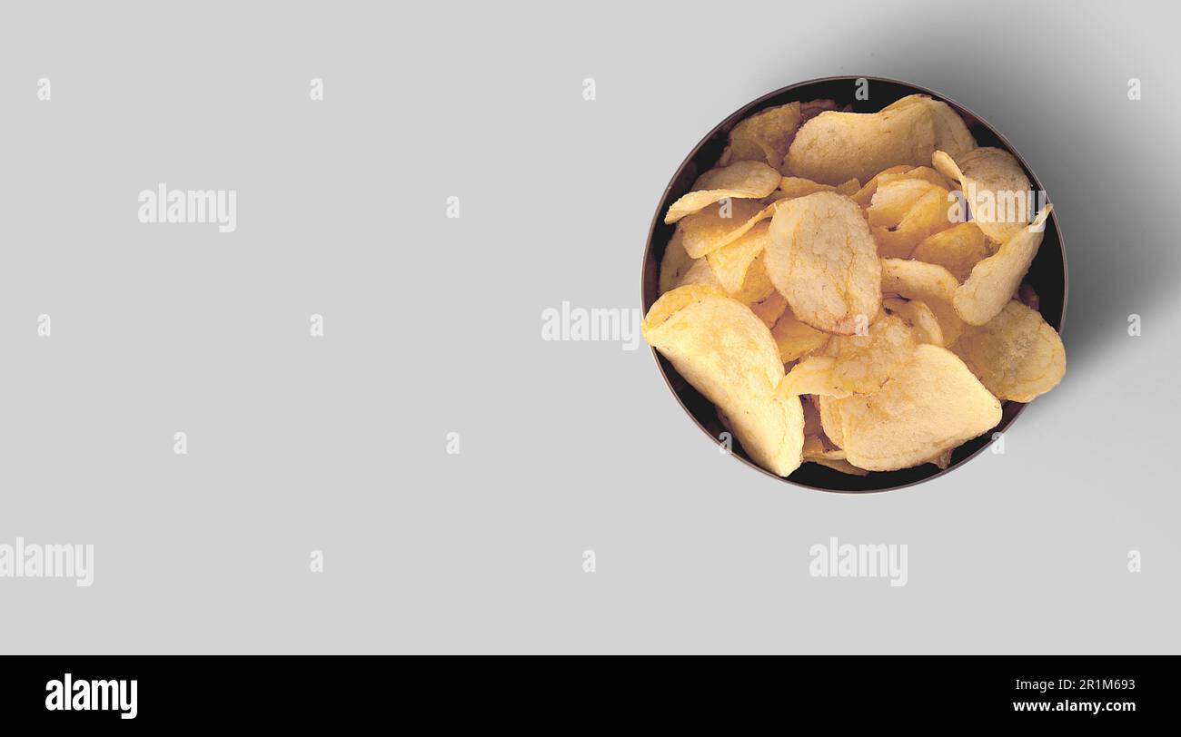 Crispy potato chips in a black ceramic tray on a grey background, top