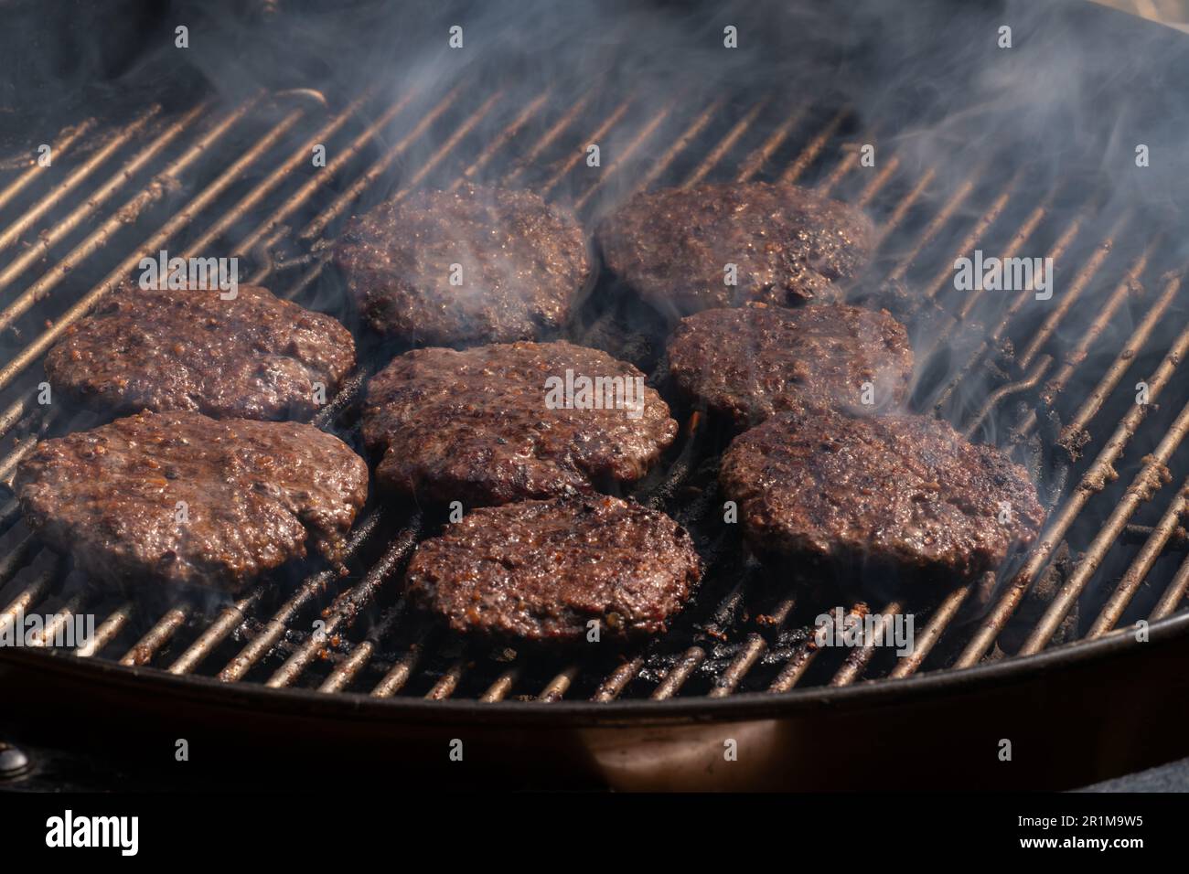 Grilling burgers on barbecue BBQ grill on hot charcoal. Homemade burger patties are being roasted on grill bars. Stock Photo