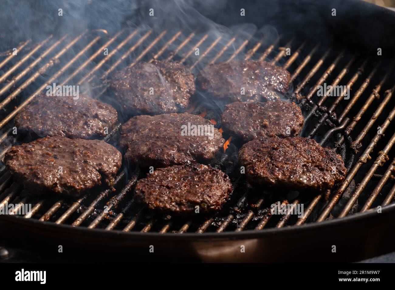 Grilling burgers on barbecue BBQ grill on hot charcoal. Homemade burger patties are being roasted on grill bars. Stock Photo