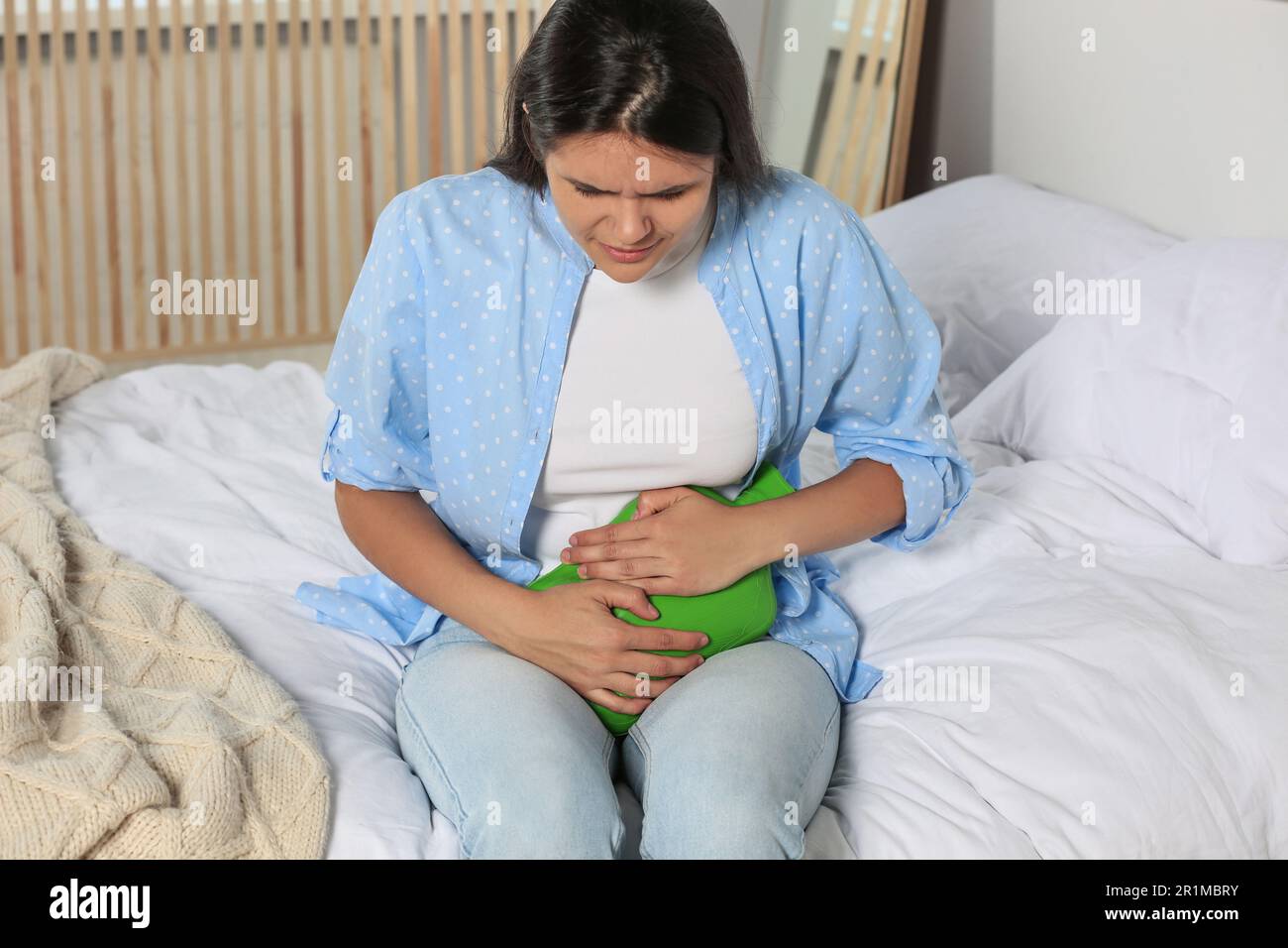 Young woman using hot water bottle to relieve cystitis pain on bed at
