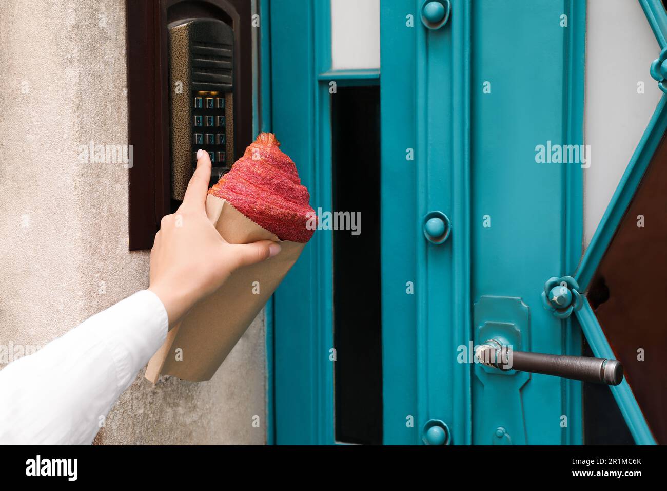 Woman with delicious croissant and ringing doorbell outdoors, closeup Stock Photo