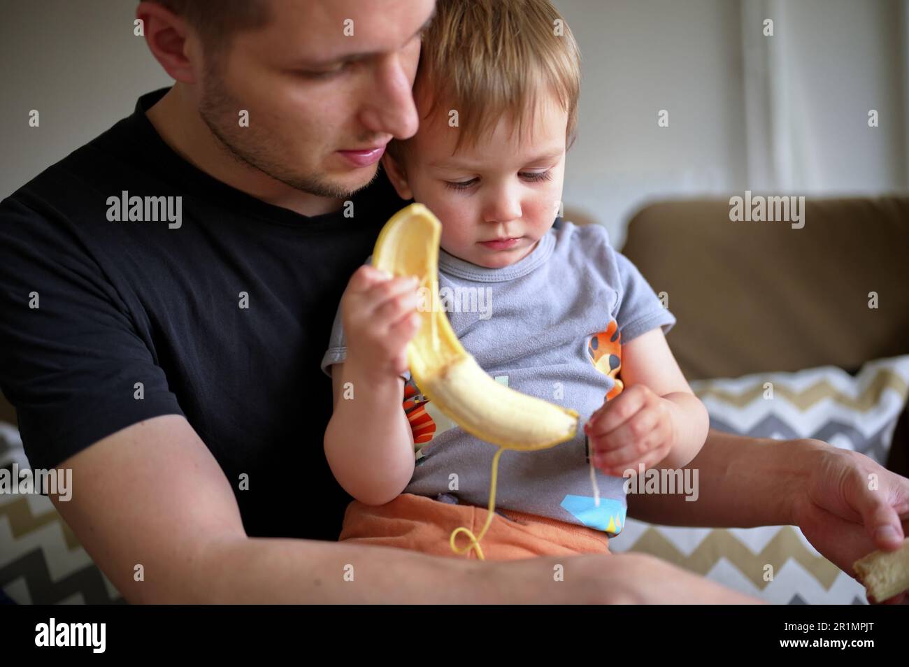 Father holding his little toddler helping him to peel banana Stock ...