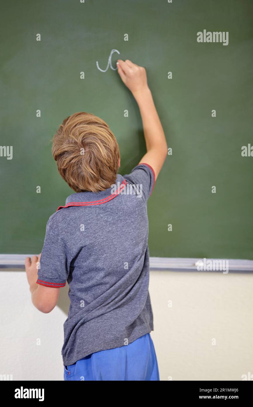 He knows the answer. A young boy writing on the blackboard at school