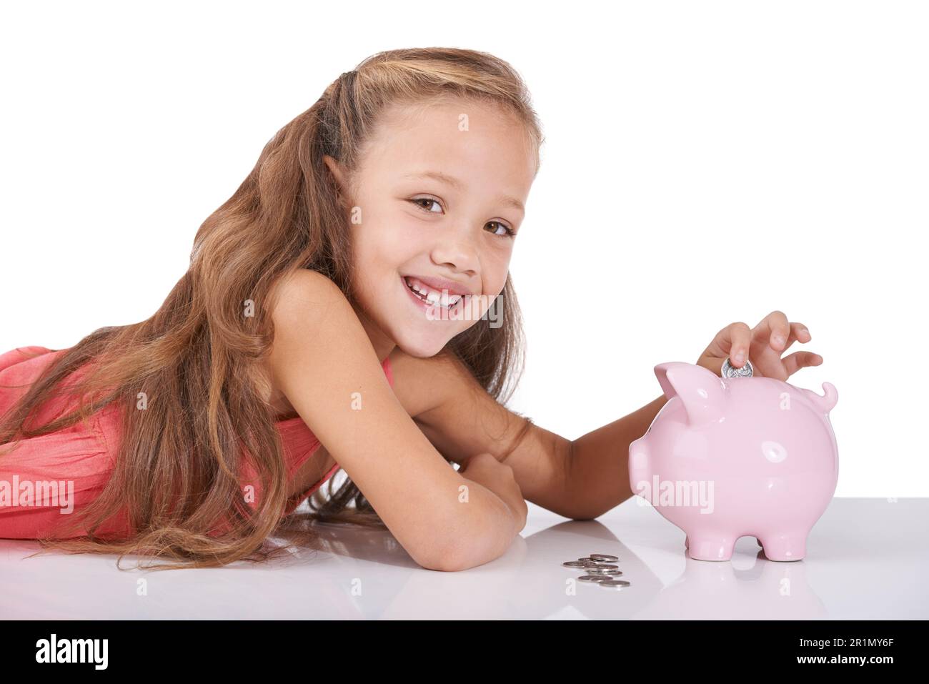 Saving starts early these days...Studio shot of a little girl smiling at the camera while putting a coin in her piggybank. Stock Photo