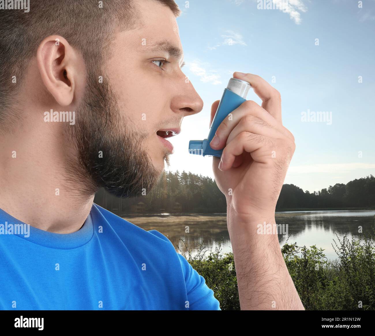 Man using asthma inhaler near lake. Emergency first aid during outdoor recreation Stock Photo