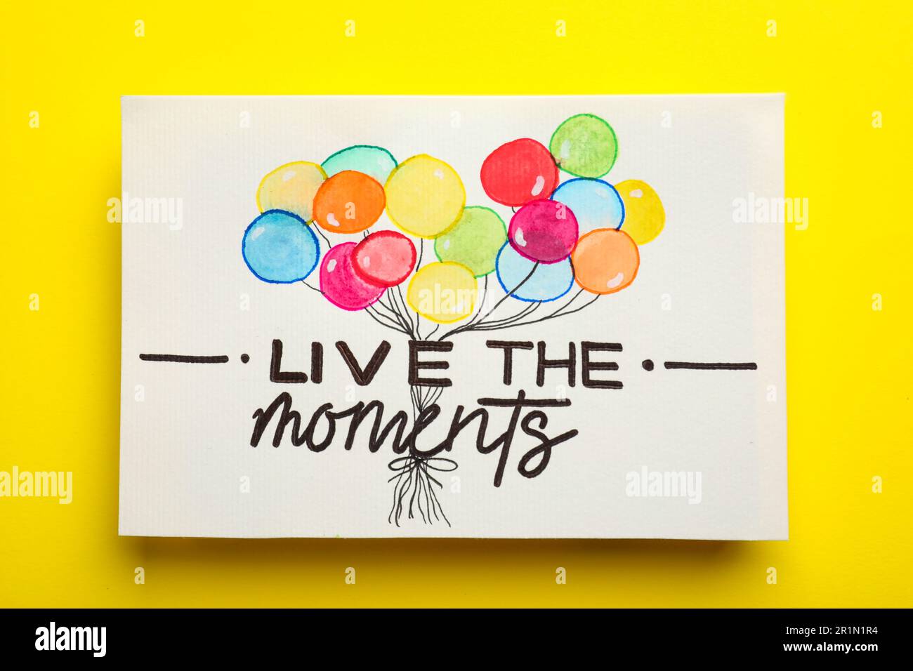 Card with life-affirming phrase Live The Moments on yellow background, top view Stock Photo