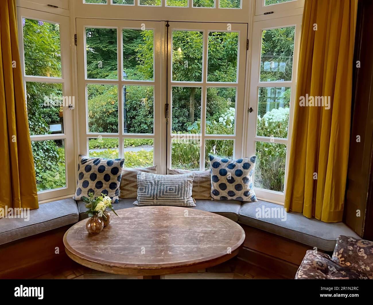 Wooden table near bay window seat with cushions in cozy room. Interior ...