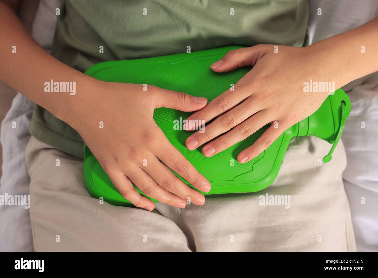 Young woman using hot water bottle to relieve cystitis pain on bed