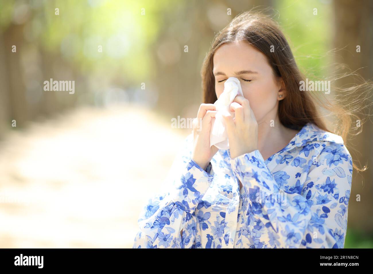 Allergic woman blowing on tissue walking in summer in a park Stock Photo