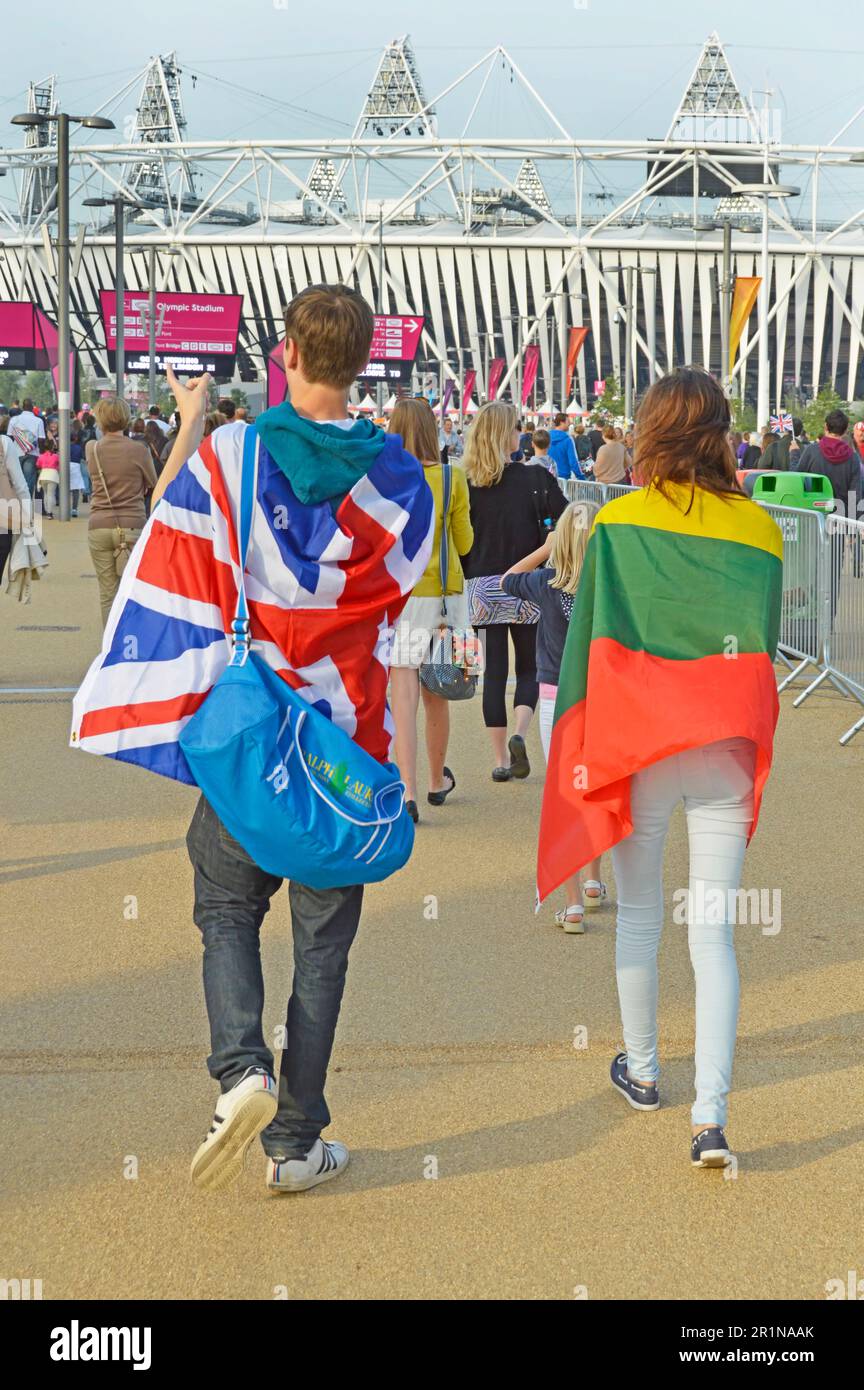 Back view young couple walk into Olympic Park main entrance for London 2012 Paralympic Games one draped in Union Jack & one in Lithuania flags in UK Stock Photo