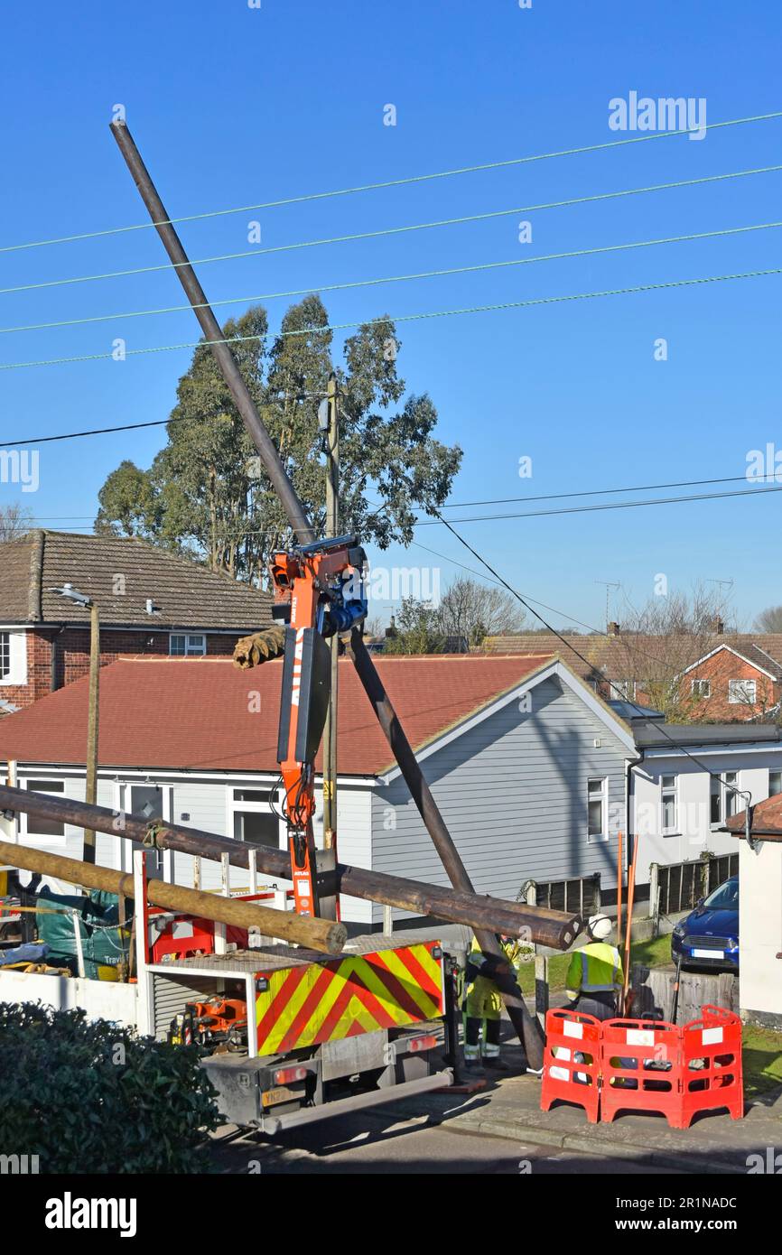 Electrical engineering contractors install new timber pole to carry replacement overhead electricity cables to houses in residential road England UK Stock Photo