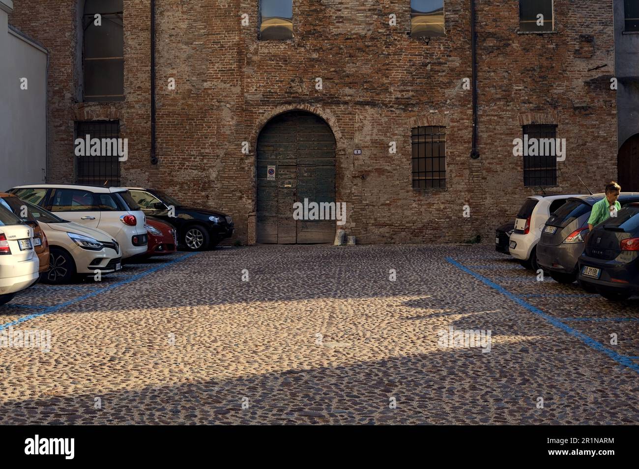Cobbled square  in the shade with parked cars in front of the facade of a building Stock Photo