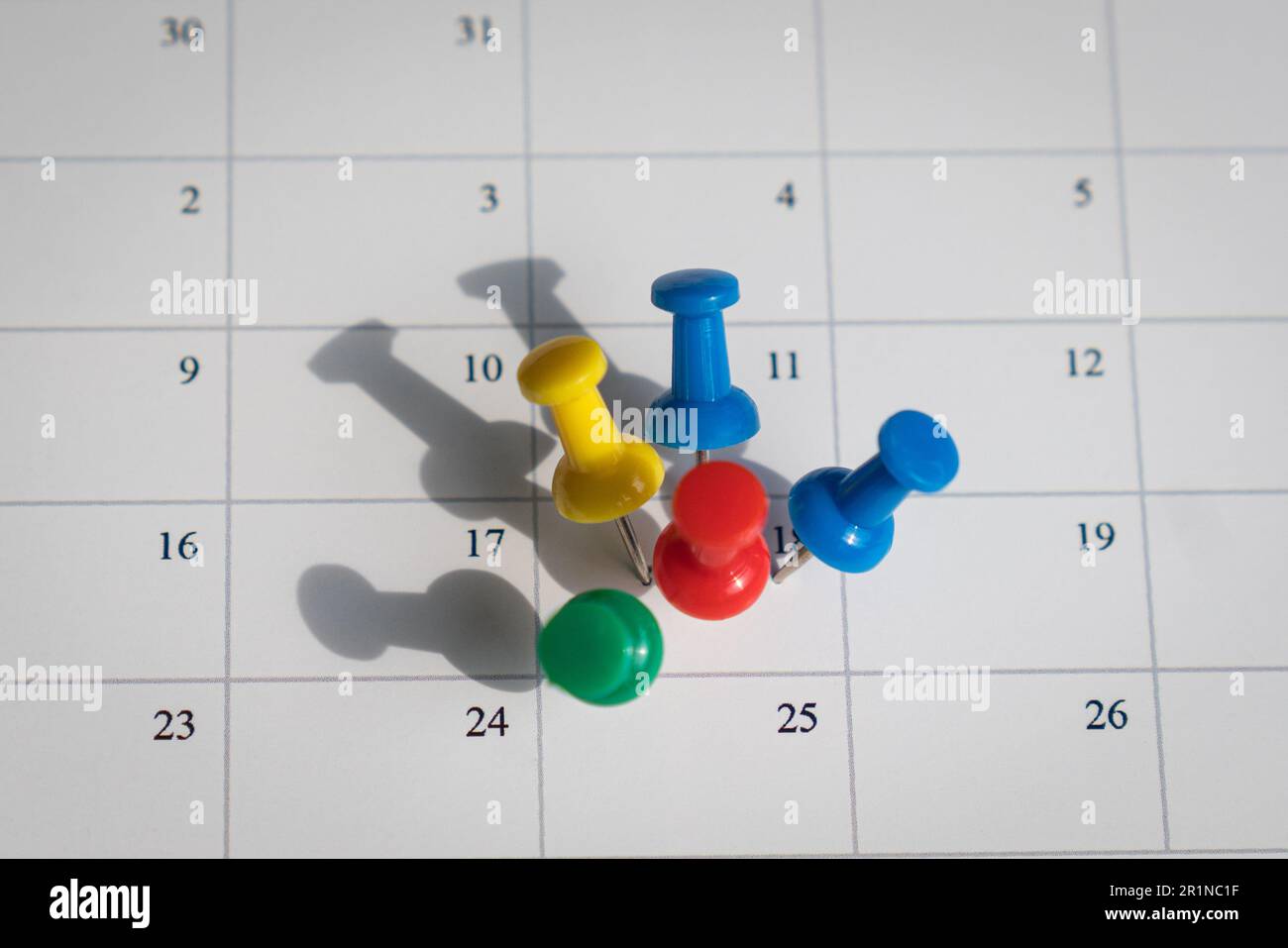 Multicolored pins on one date on a calendar. Busy and fully booked schedule concept. Stock Photo