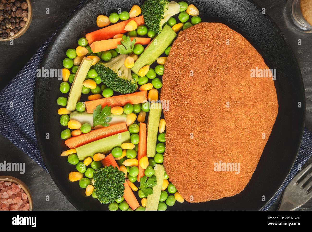 Fried Chicken Schnitzel served with delicious sautéed vegetables on dark wooden background. Stock Photo