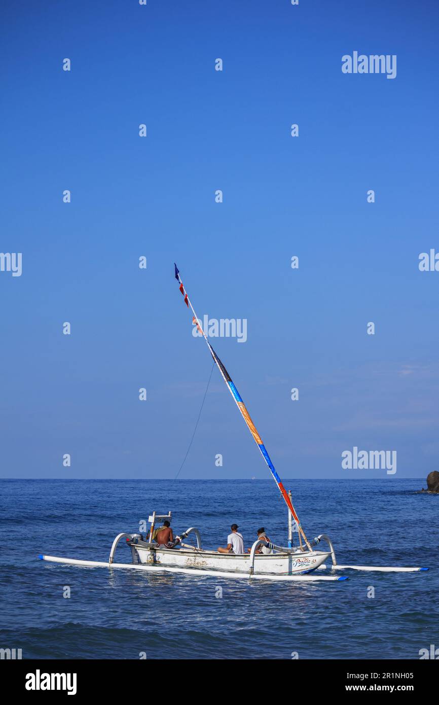 A group of people riding in a white Balinese fishing boat with a ...