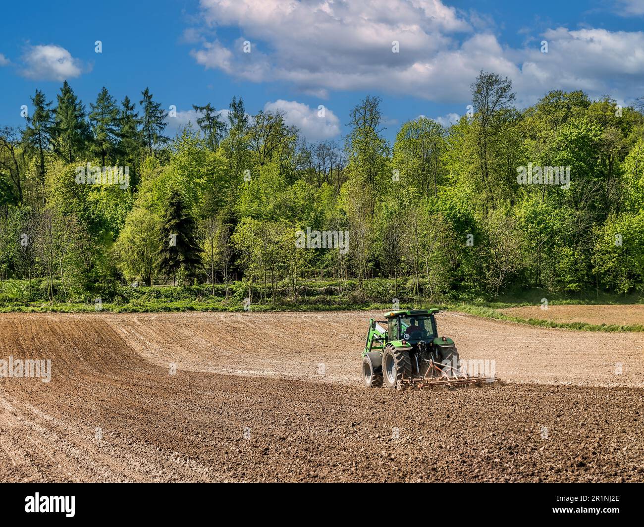 A shot of farm tractor harrowing arable field Stock Photo