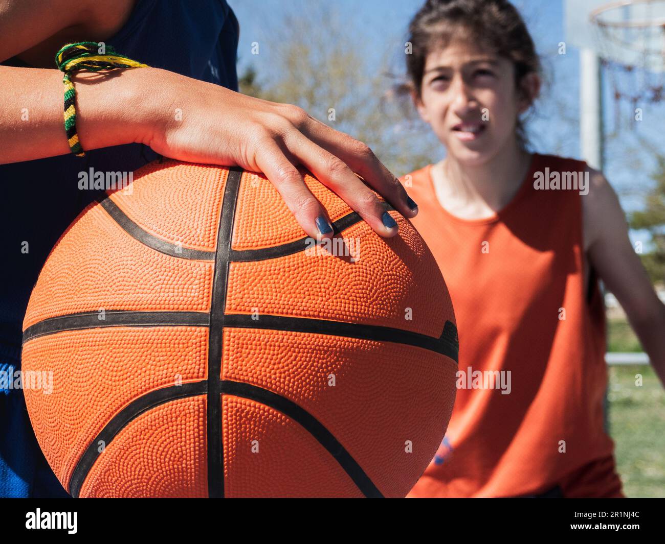 Close-up of a basketball picked up by a boy performing a one-on-one on an outdoor court. Stock Photo