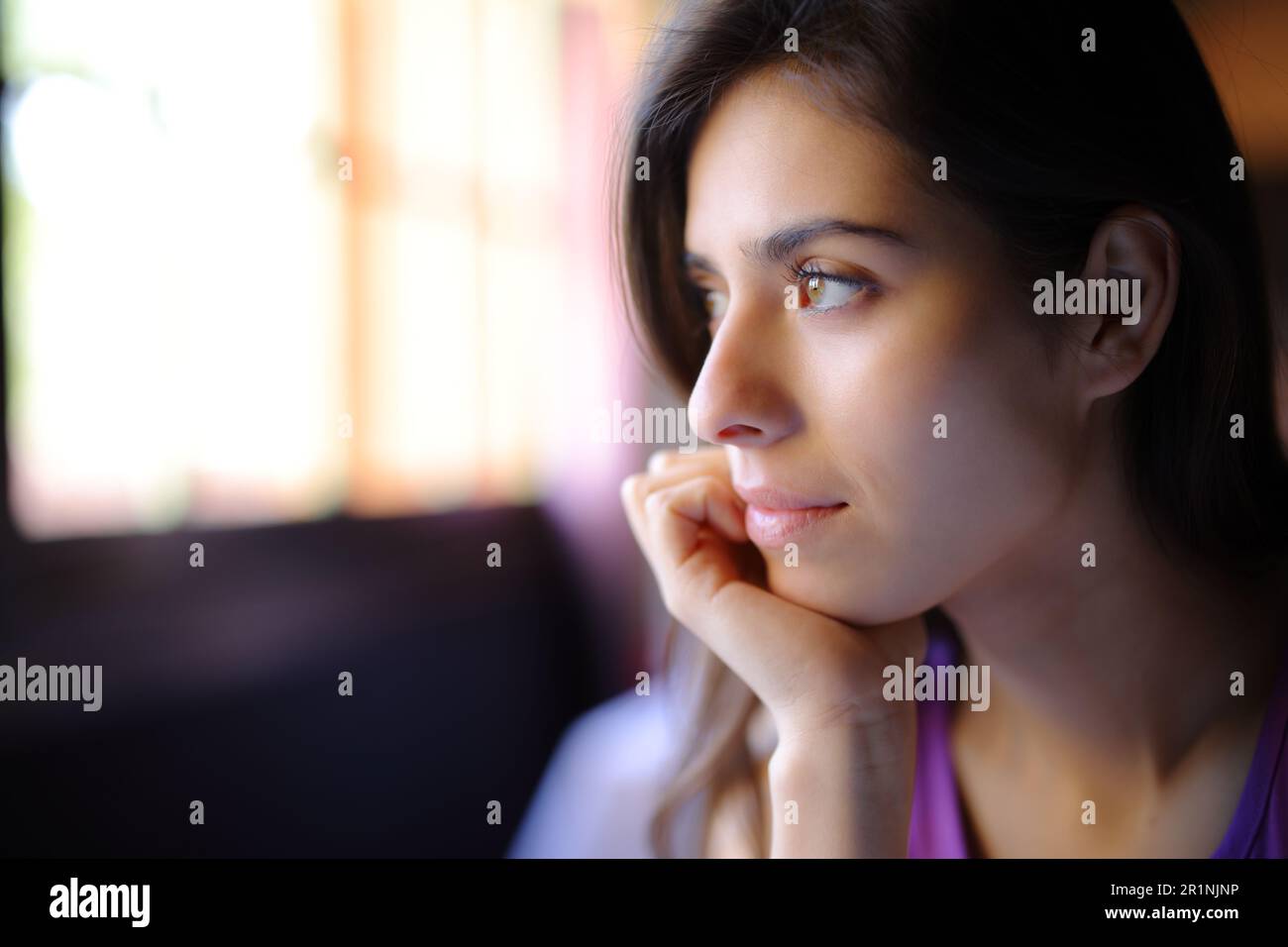 Beautiful woman relaxing looking through a window in a house interior Stock Photo