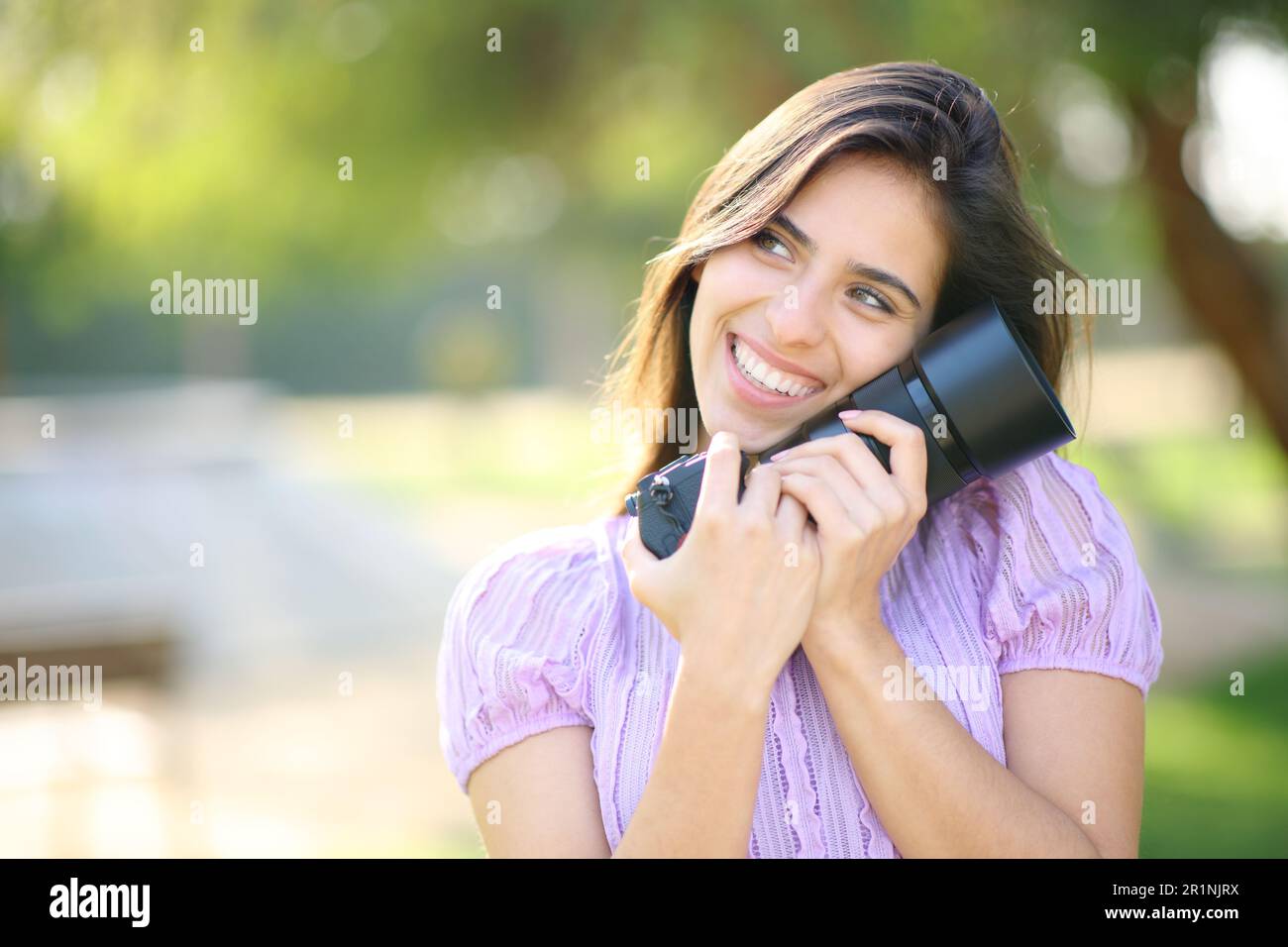 Happy photographer loving her new camera standing in a park Stock Photo