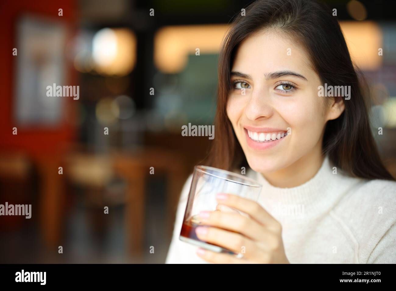 Happy woman holding soda glass in a bar looking at you Stock Photo