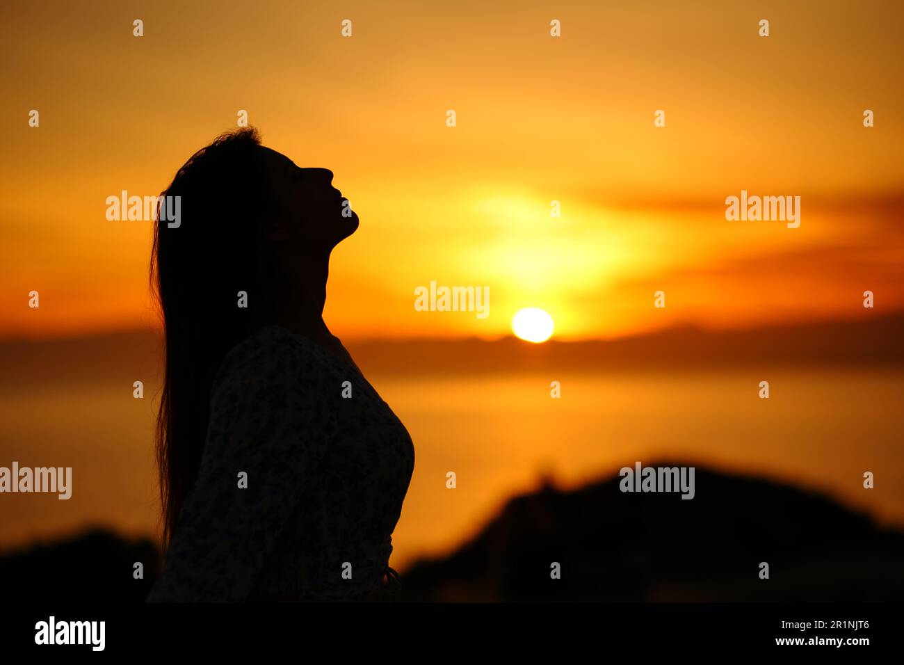Side view portrait of a silhouette of a woman breathing at sunset or sunrise on the beach Stock Photo