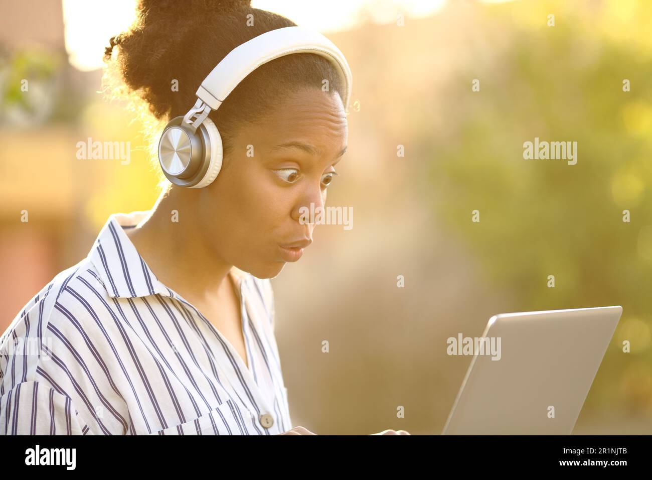 Surprised black woman watching media on laptop in a park Stock Photo