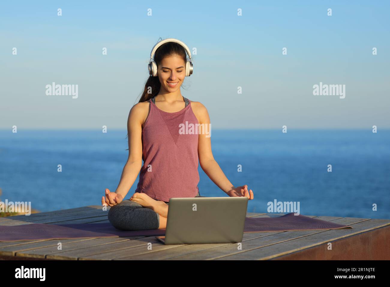 Yogi doing yoga watching video tutorial online on laptop on the beach Stock Photo