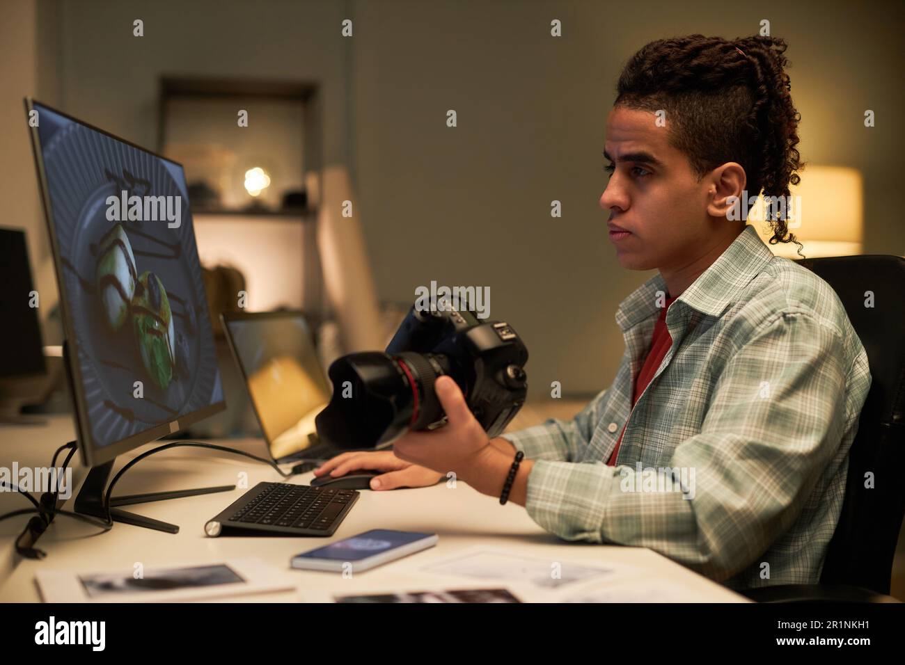 Young photographer sitting at his workplace with camera and retouching ...
