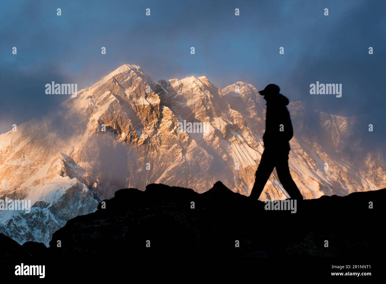 A man walks in silhouette on a ridge with Nuptse in the Himalayan background at sunset. Stock Photo