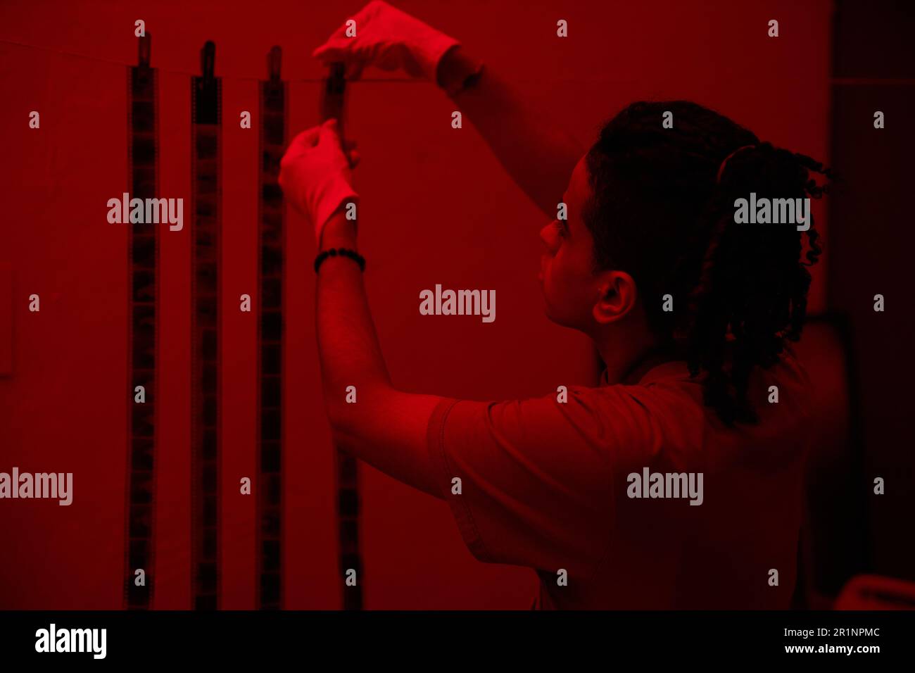 Young photographer hanging photo film during his work in darkroom with