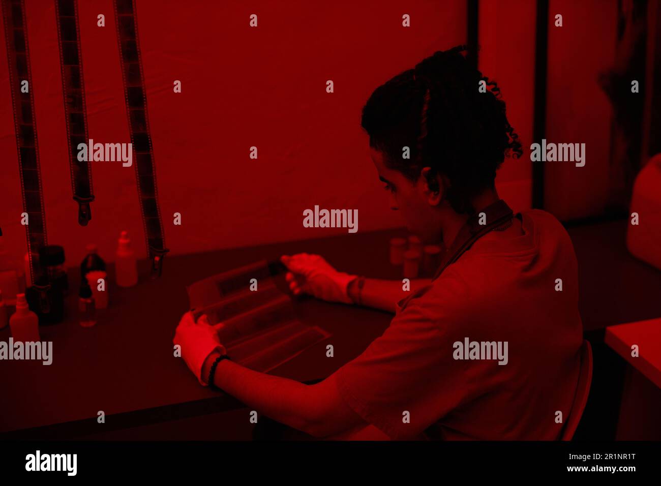 Young photographer working with photo film at table in darkroom with