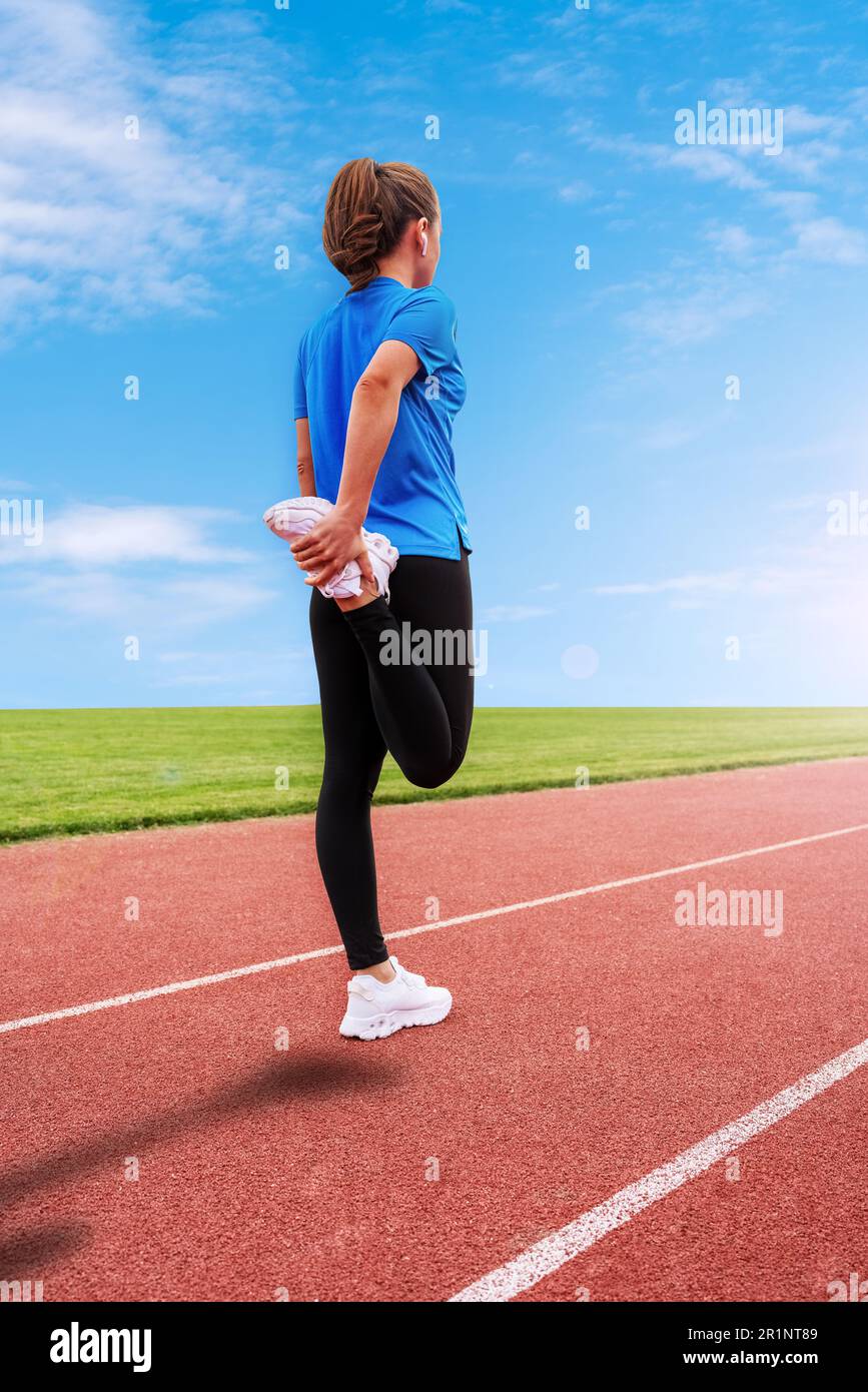 Female athlete standing on running track before start line warming up