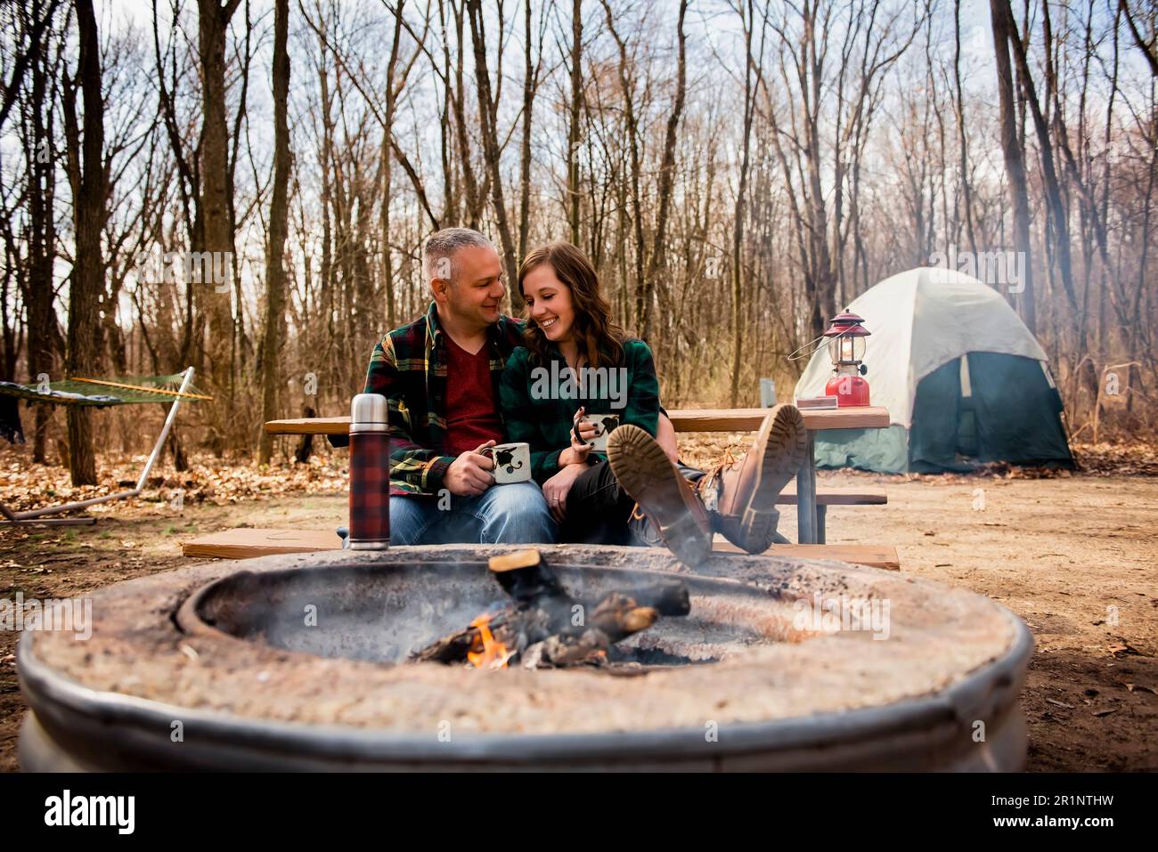 Smiling couple relaxes by campfire drinking coffee in Fall Stock Photo