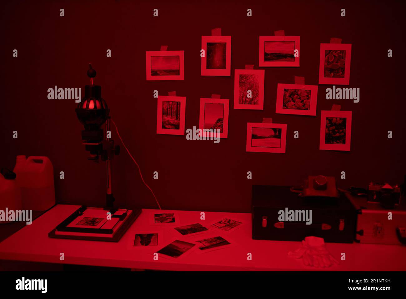 Workplace with equipment and photos on table in darkroom with red light
