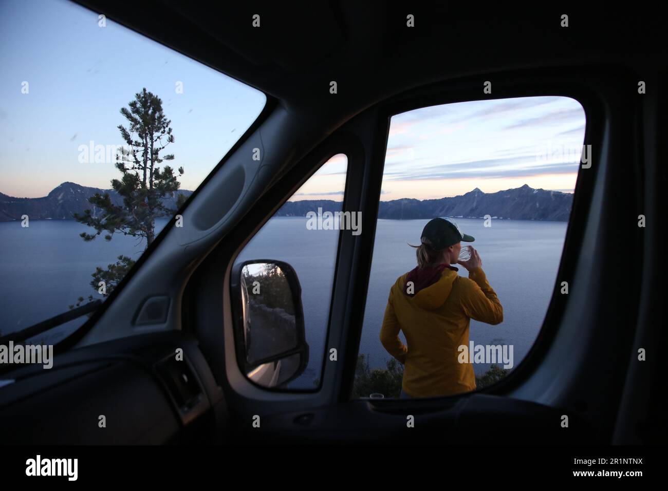 Ayoung woman enjoys a drink on the edge of Crater Lake National Park. Stock Photo