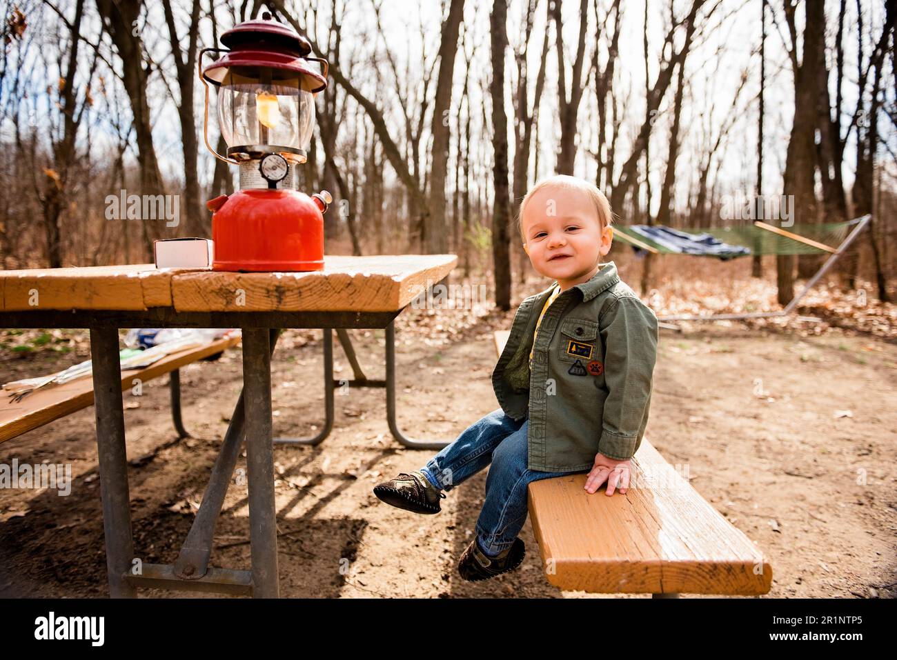 Smiling toddler boy sits on picnic table at campsite in fall Stock Photo