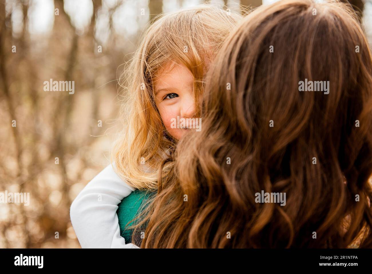 Smiling girl peeks over mothers shoulder outside in Fall woods Stock Photo