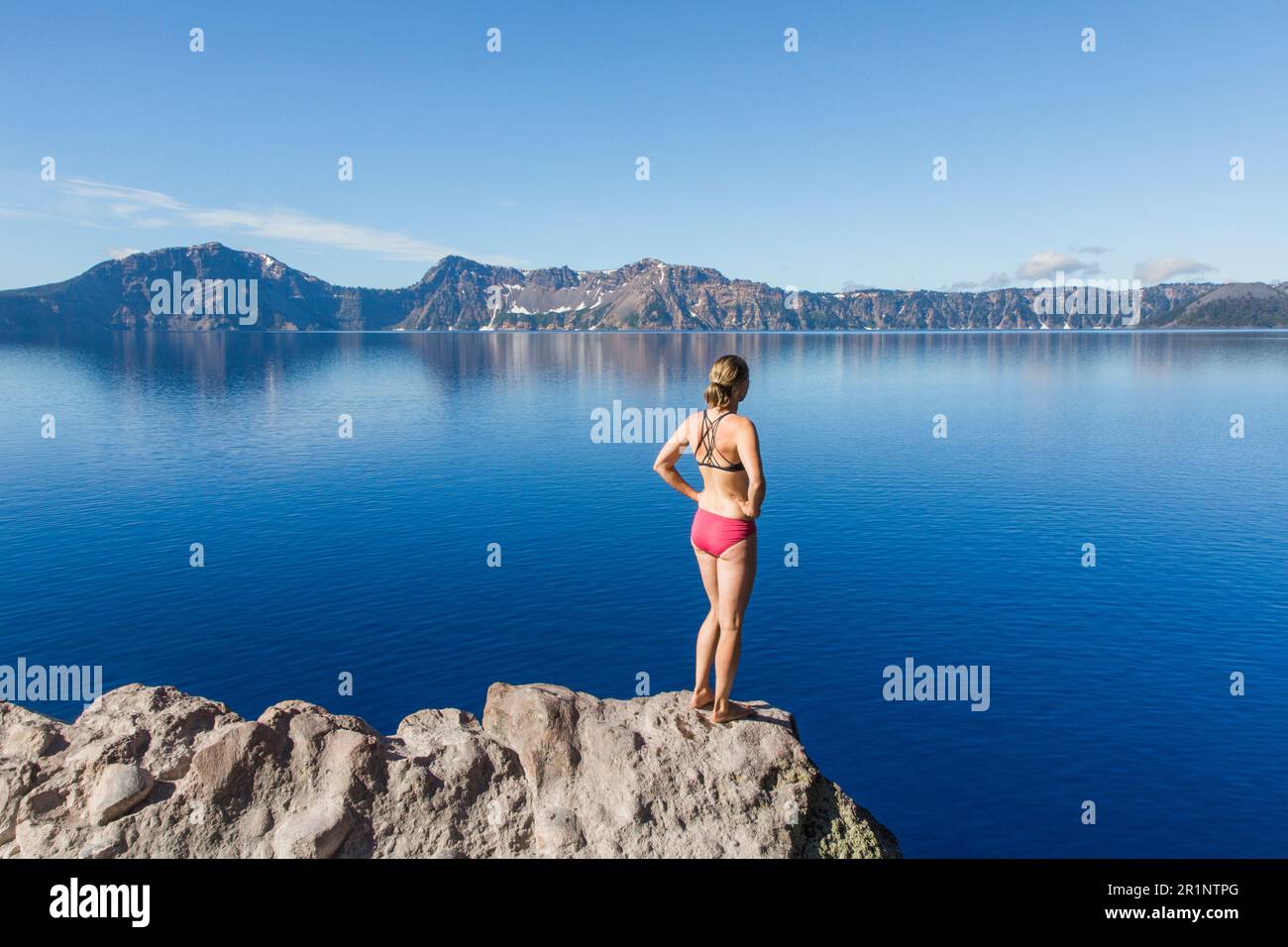 A young woman stands on the rim of Crater Lake. Stock Photo