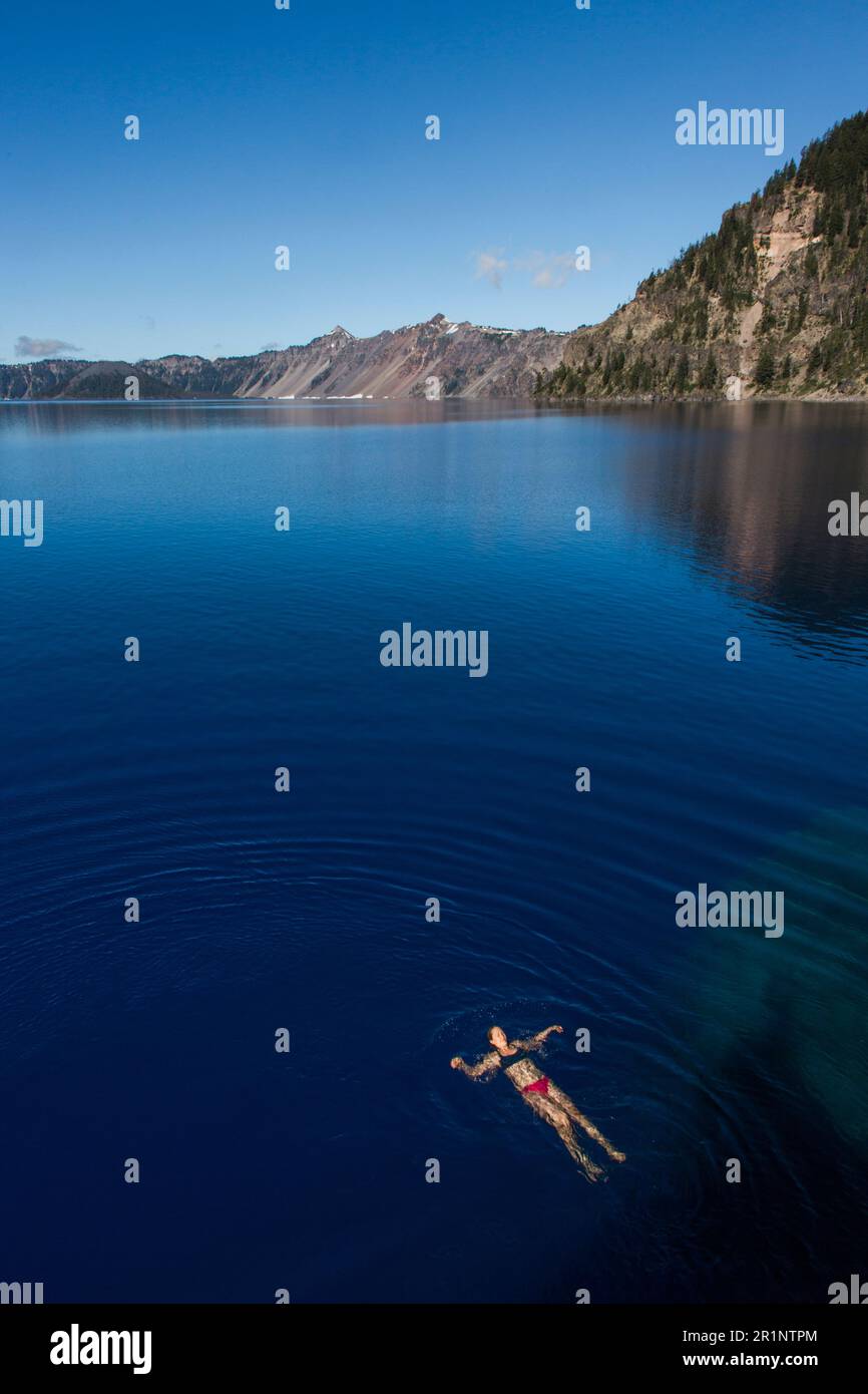 A young woman swims in the cold, clear waters of Crater Lake. Stock Photo