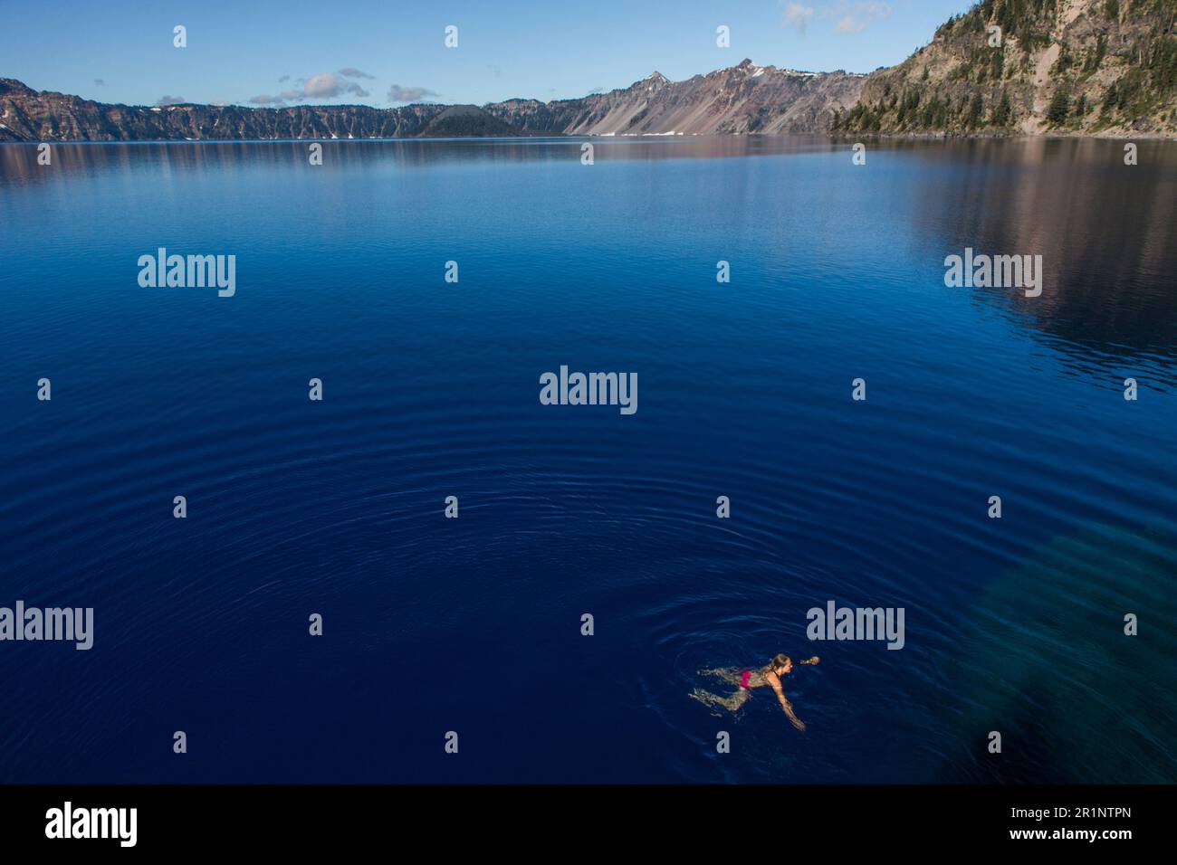 A young woman swims in the cold, clear waters of Crater Lake. Stock Photo
