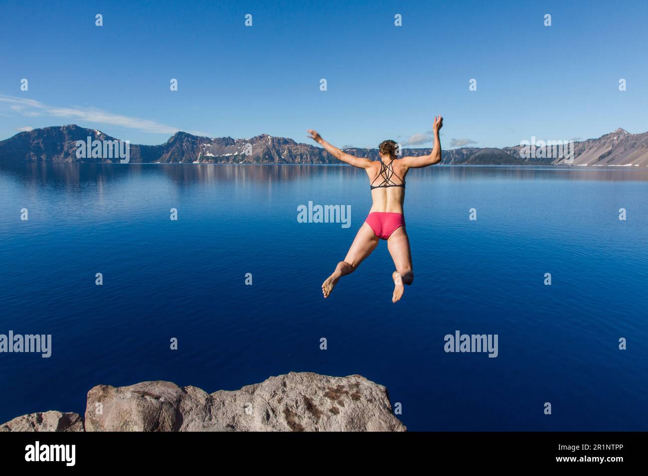 A young woman jumps in the cold, clear waters of Crater Lake. Stock Photo