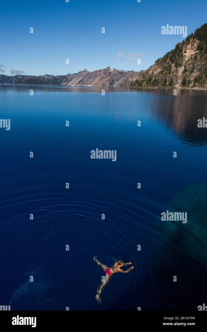 A young woman swims in the cold, clear waters of Crater Lake. Stock Photo