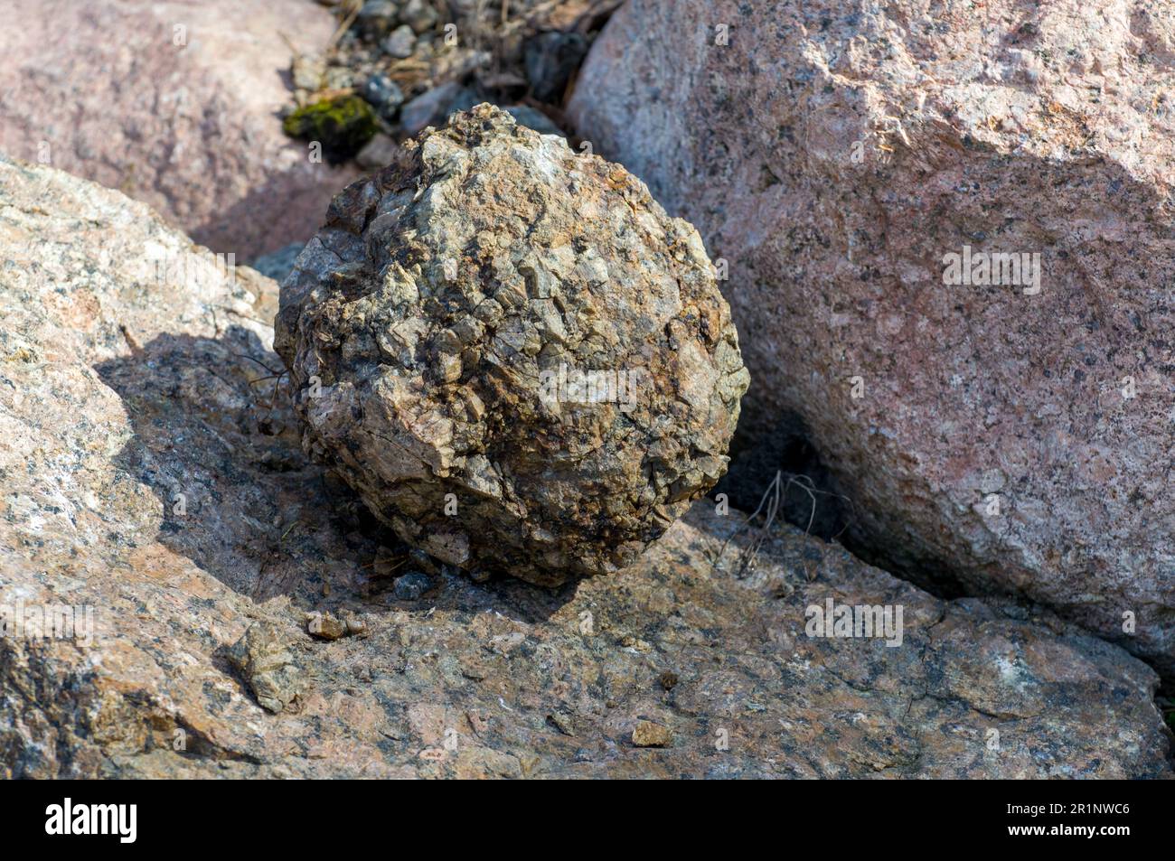 A round natural stone on top of larger stones. Illuminated by sunlight ...