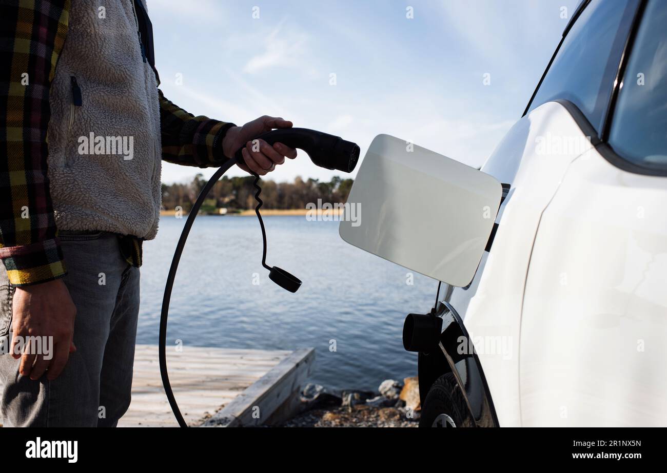 person plugging in an electric car by the sea in Sweden Stock Photo