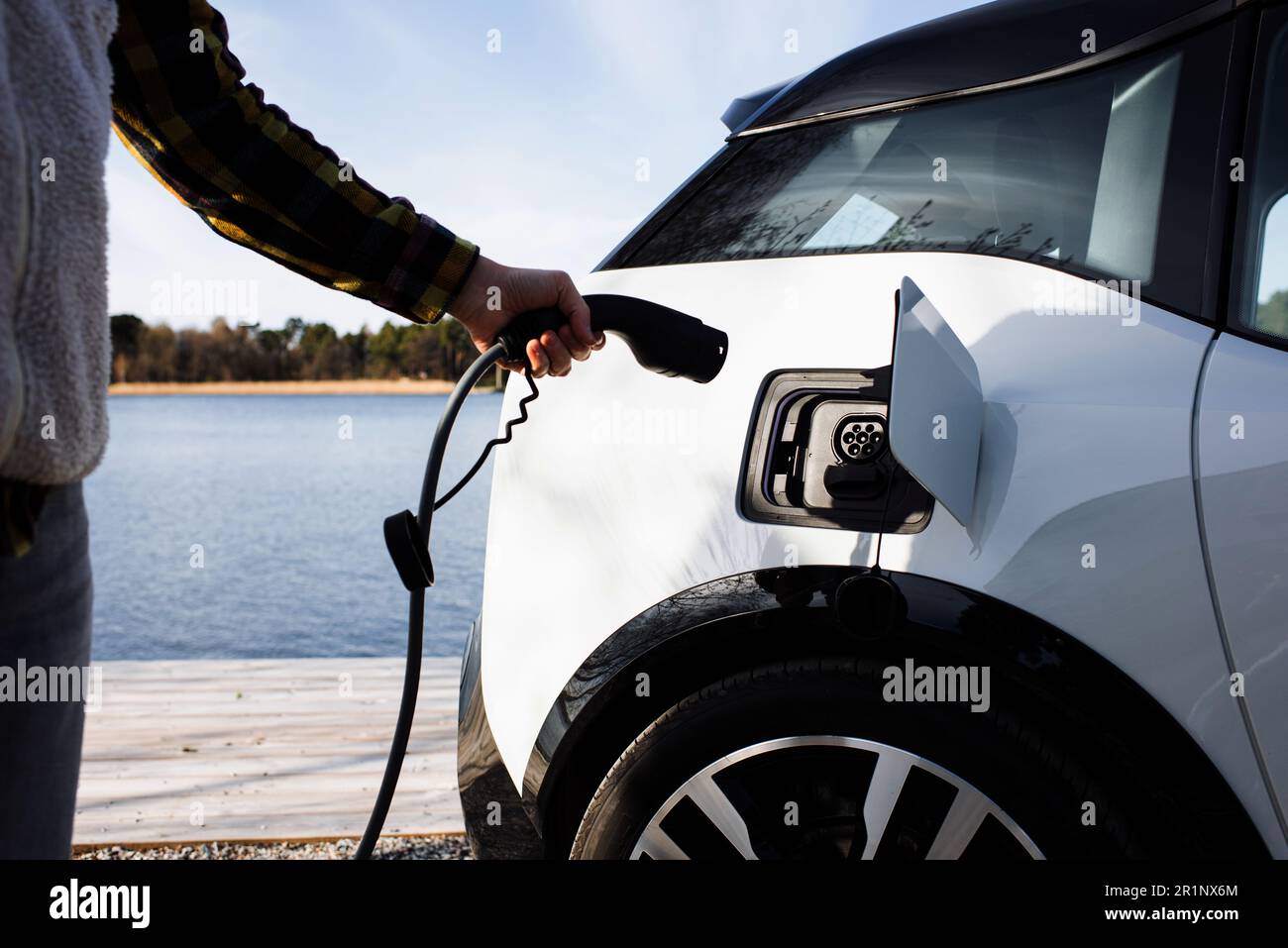 Person plugging in an electric car by the water in Stockholm Stock Photo